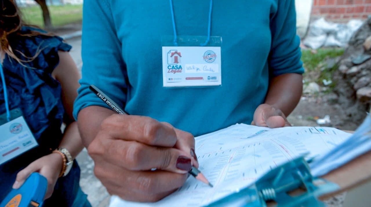 Técnica da equipe preenchendo uma ficha cadastral em campo, com crachá de identificação